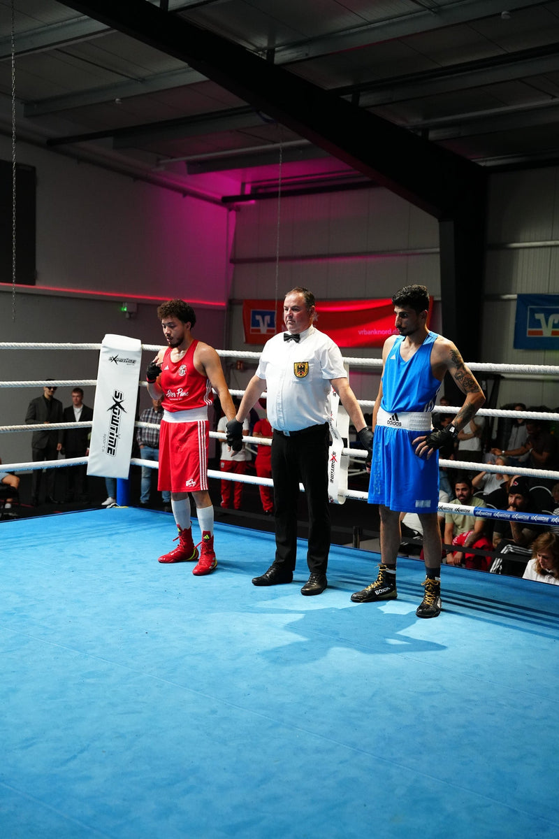 Ringrichter steht mit zwei Boxern im Ring bei einer Boxveranstaltung