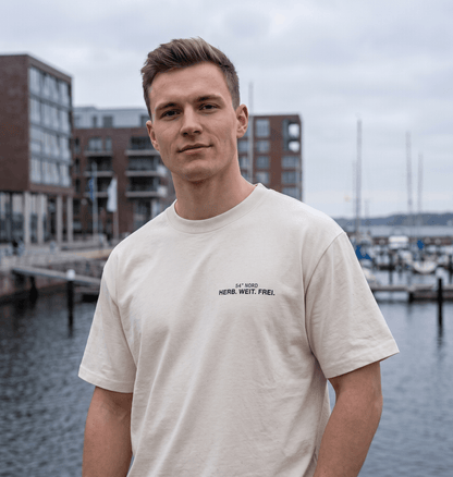 Junger Mann trägt das Herb. Weit. Frei. Oversized T-Shirt in Gischt mit kleinem 54° Nord Brustprint am Hafen.