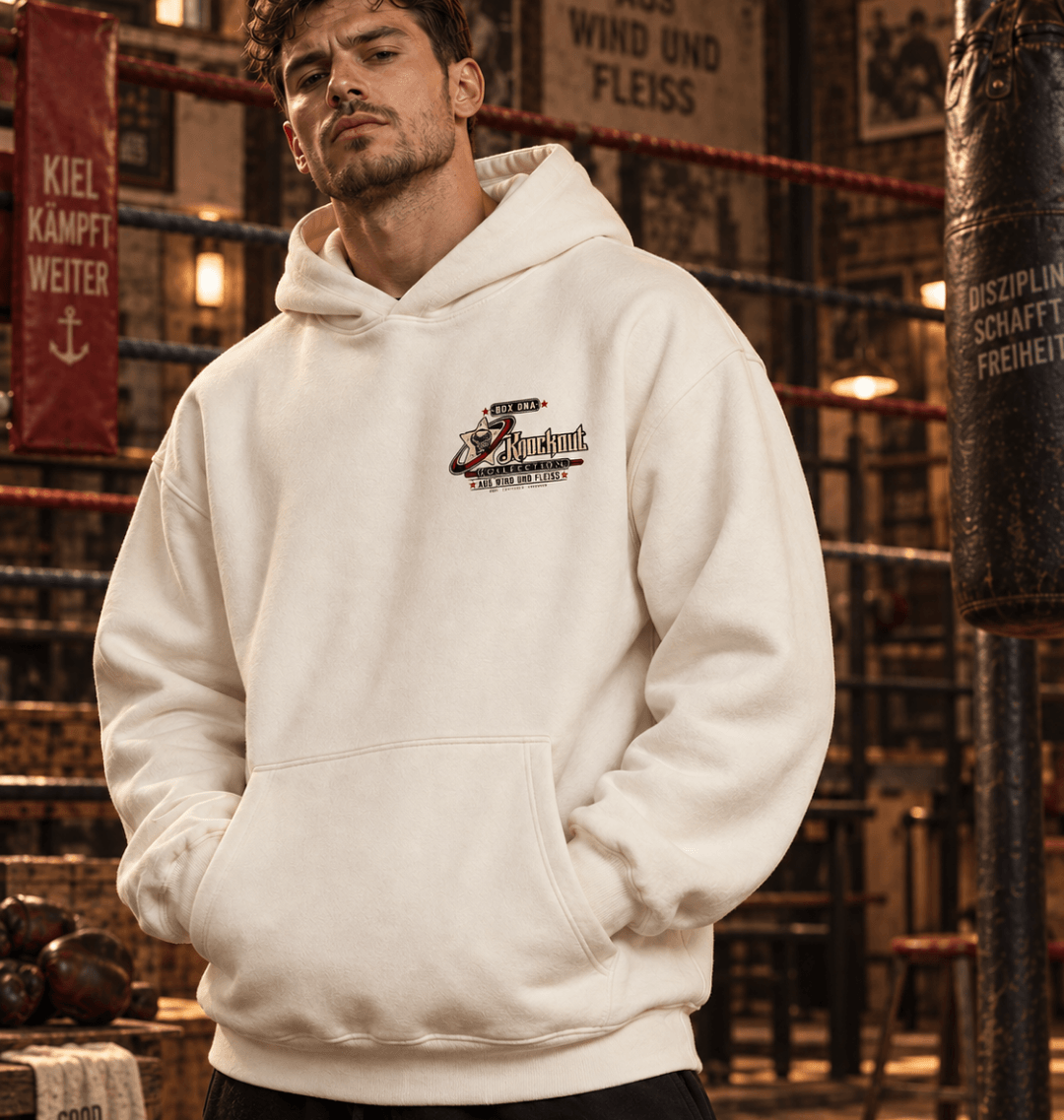 Mann trägt Natural Raw Ultra Heavy Hoodie 10–9 mit kleinem Box-DNA-Frontprint in einer Boxhalle