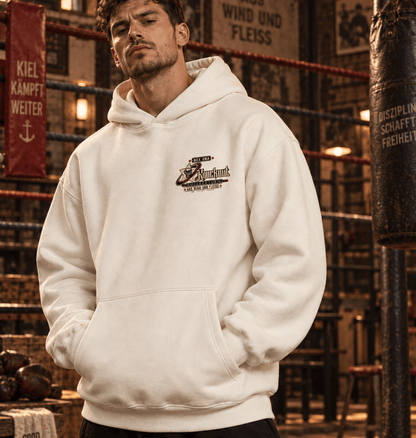 Mann trägt Natural Raw Ultra Heavy Hoodie 10–9 mit kleinem Box-DNA-Frontprint in einer Boxhalle